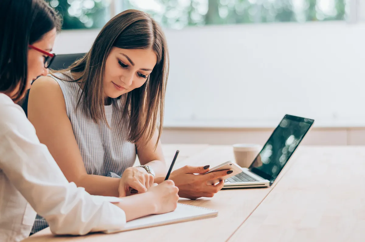 Zwei Frauen lernen gemeinsam am Tisch mit Laptop und Notizblock