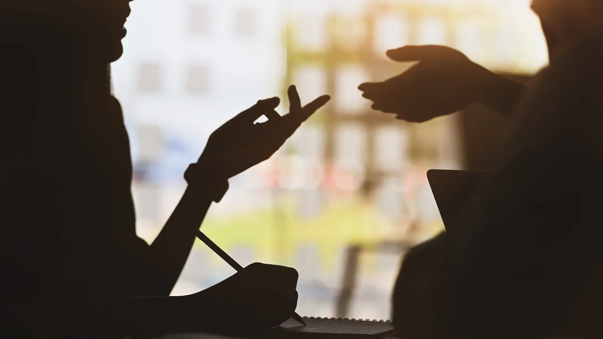 Zwei Personen im Gespräch als Silhouetten vor einem Fenster